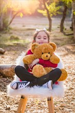 Cute young mixed-race girl hugging teddy bear outdoors