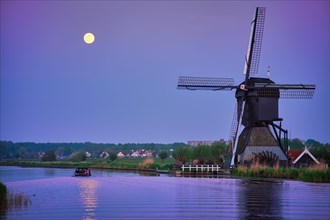 Netherlands rural landscape with windmills at famous tourist site Kinderdijk in Holland in twilight with full moon and boat in canal