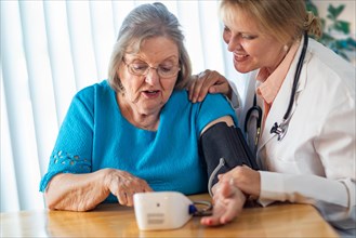 Senior adult woman learning from female doctor to use blood pressure machine