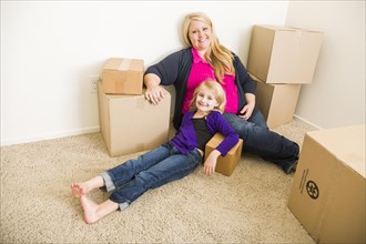 Happy young mother and daughter in empty room with moving boxes