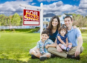 Young family with children in front of custom home and sold for sale real estate sign