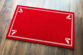 Blank holiday red welcome mat with holly corners on wood floor background