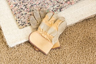 Construction gloves on pulled back carpet and underlay in room