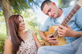 Young adult man playing guitar for his girlfriend in the park