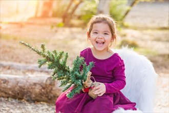 Cute mixed-race young baby girl holding small christmas tree outdoors