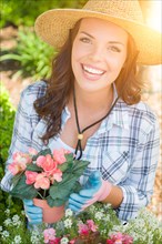 Happy young adult woman wearing hat and gloves gardening outdoors