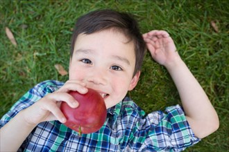 mixed-race chinese and caucasian young boy with apple relaxing on his back outside on the grass