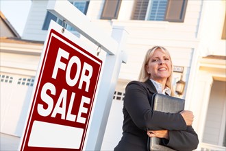 Female real estate agent in front of for sale sign and beautiful house