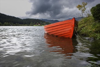 Leeres rote Ruderboot am Seeufer bei Regenwetter