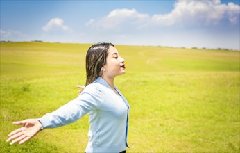 Happy woman breathing fresh air in the field and spreading arms