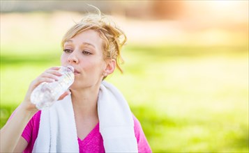 Young fit adult woman outdoors with towel drinking from her water bottle