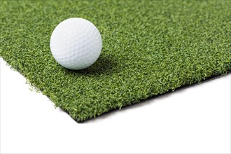 Golf ball resting on section of artificial turf grass on white background