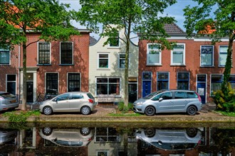 Cars and bicycles parked along the canal in street of Delft with reflection. Delft