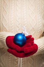 Woman wearing seasonal red mittens holding blue christmas ornament
