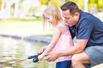 Young caucasian father and daughter having fun fishing at the lake