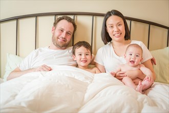 mixed-race chinese and caucasian baby boys laying in bed with their father and mother