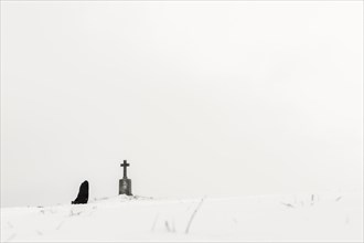 Einsame Frau knieend an Marterl in Winterlandschaft