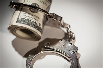 Handcuffs locked on roll of one hundred dollar bills under spotlight