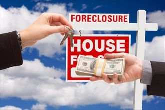 Handing over cash for house keys in front of foreclosure sign and cloudy blue sky