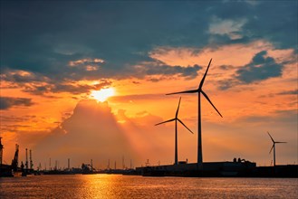 Wind turbines power electricity generators in Antwerp port on sunset