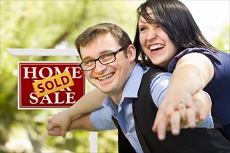 Happy attractive caucasian couple in front of sold real estate sign