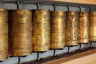 Rotating motion blurred metal buddhist prayer wheels with Om Mani Padme Hum mantra meaning Praise to Jewel in Lotus in Tsuglagkhang complex in Dalai Lama residence