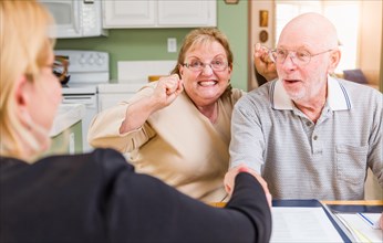 Senior adult couple celebrating over documents in their home with agent at signing