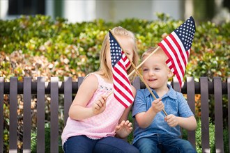 Young sister and brother waving american flags on the bench at the park