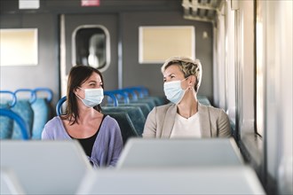 A couple of friends wearing mask and nicely talking while traveling by train