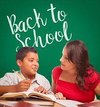 Back to school written on chalk board behind hispanic young boy and famale adult studying