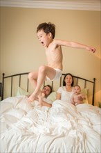 Young mixed-race chinese and caucasian boy jumping in bed with his family