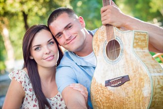 Young adult couple portrait with guitar in the park