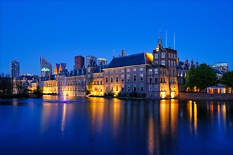 View of the Binnenhof House of Parliament and the Hofvijver lake with downtown skyscrapers in background illuminated in the evening