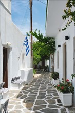 Picturesque narrow street with traditional whitewashed houses with greek flag of Naousa town in famous tourist attraction Paros island