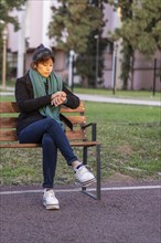 Latin woman sitting on a bench in a park looking at the time