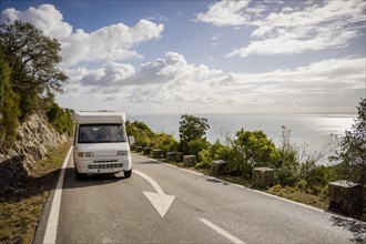 Small camper van driving on scenic road with sea views in Arrabida Natural Park