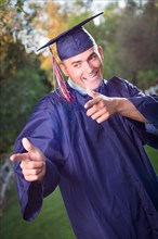 Happy handsome male graduate in cap and gown outside