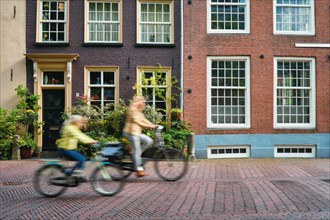 Motion blurred bicycle rider cyclist woman and child on bicycle very popular means of transport in Netherlands in street with old houses of Delft