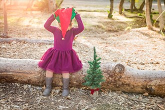 Cute mixed-race young baby girl having fun with christmas hat and tree outdoors