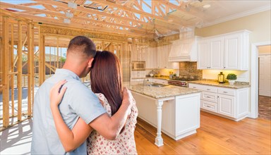 Young military couple facing house construction framing gradating into finished kitchen build