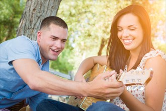 Handsome young man teaching mixed-race girl to play guitar at the park
