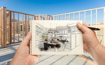 Male hands holding pen and pad of paper with custom kitchen illustration inside construction framing