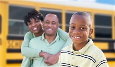 Proud african american parents and young boy near school bus