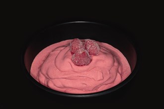 Three frozen raspberries on a raspberry ice cream in a black porcelain bowl