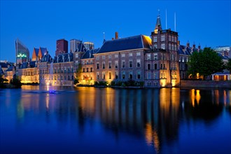 View of the Binnenhof House of Parliament and the Hofvijver lake with downtown skyscrapers in background illuminated in the evening
