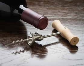 Abstract wine bottle and corkscrew laying on a reflective wood surface