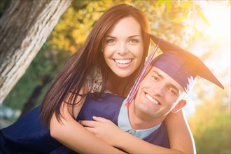Happy male graduate in cap and gown and pretty girl celebrate outside