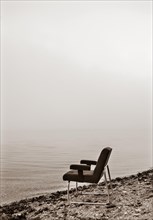 Verlassener Stuhl steht am Seeufer im Morgennebel