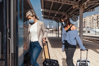 Two women in protective masks getting on the train with luggage
