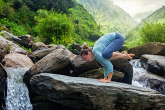 Woman doing Bakasana asana crane pose arm balance outdoors at waterfall